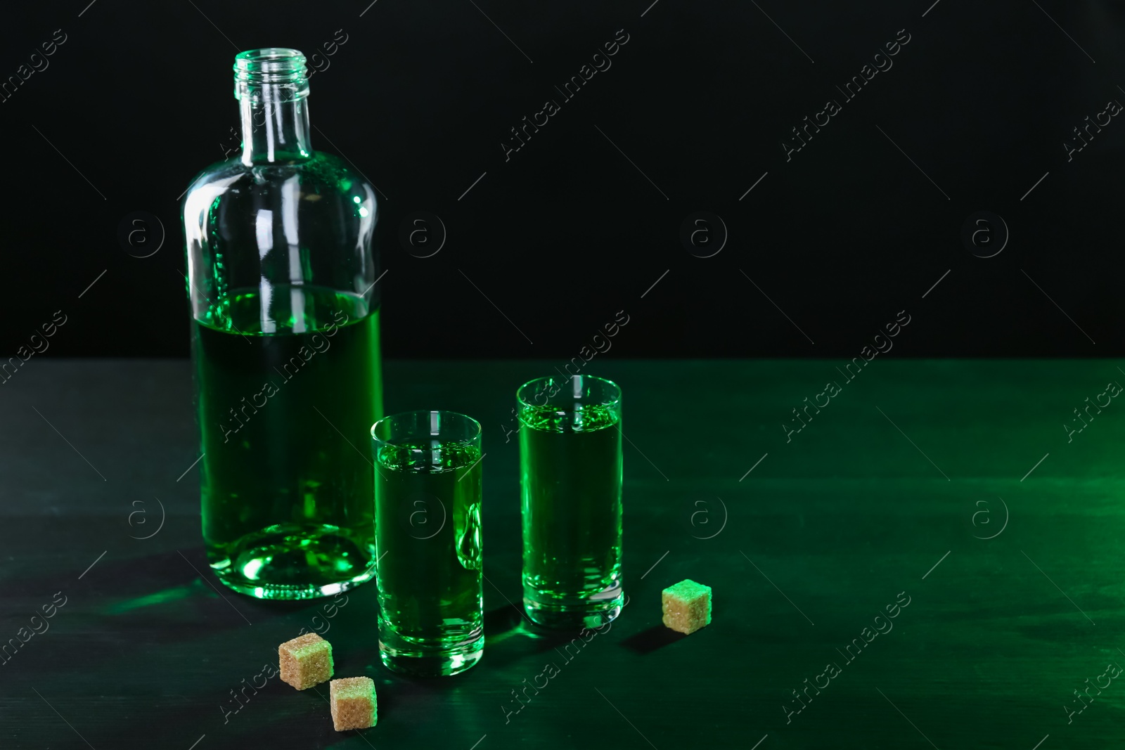 Photo of Absinthe in shot glasses, bottle and brown sugar on table, space for text