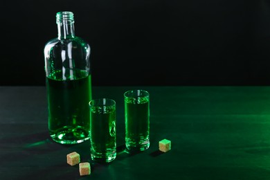 Photo of Absinthe in shot glasses, bottle and brown sugar on table, space for text