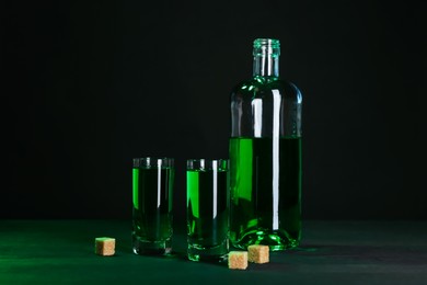 Photo of Absinthe in shot glasses, bottle and brown sugar on table against black background