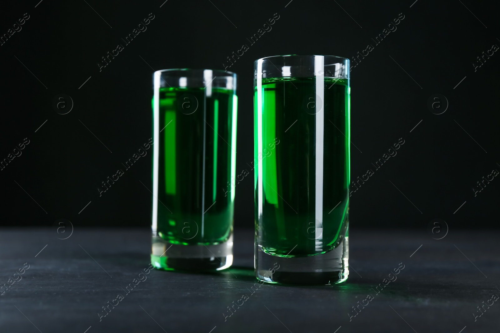 Photo of Absinthe in shot glasses on table against black background, closeup