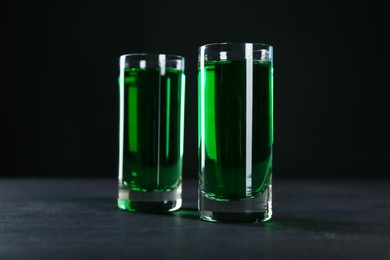 Photo of Absinthe in shot glasses on table against black background, closeup