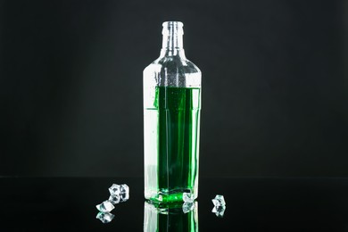 Photo of Absinthe in bottle and ice cubes on black mirror surface