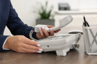 Photo of Technical support call center. Operator dialing number on telephone at wooden table indoors, closeup