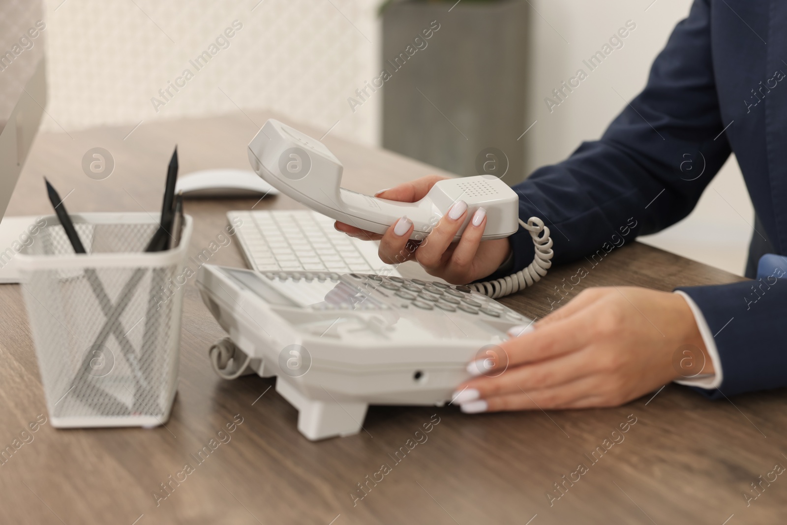 Photo of Technical support call center. Operator dialing number on telephone at wooden table indoors, closeup