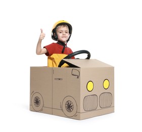 Photo of Little boy showing thumbs up while driving car made of cardboard on white background