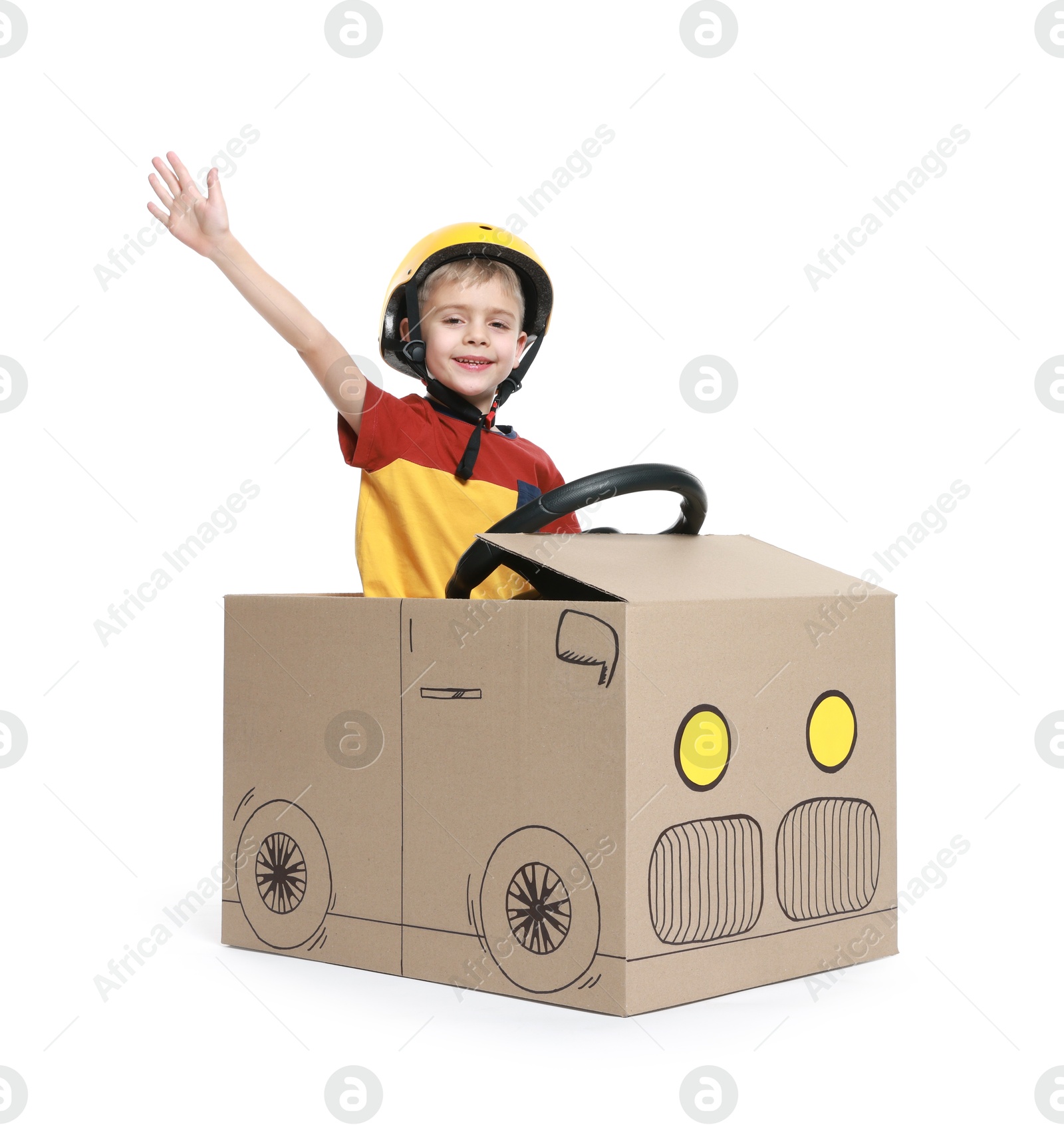 Photo of Little boy waving while driving car made of cardboard on white background