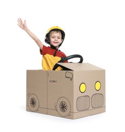 Photo of Little boy waving while driving car made of cardboard on white background