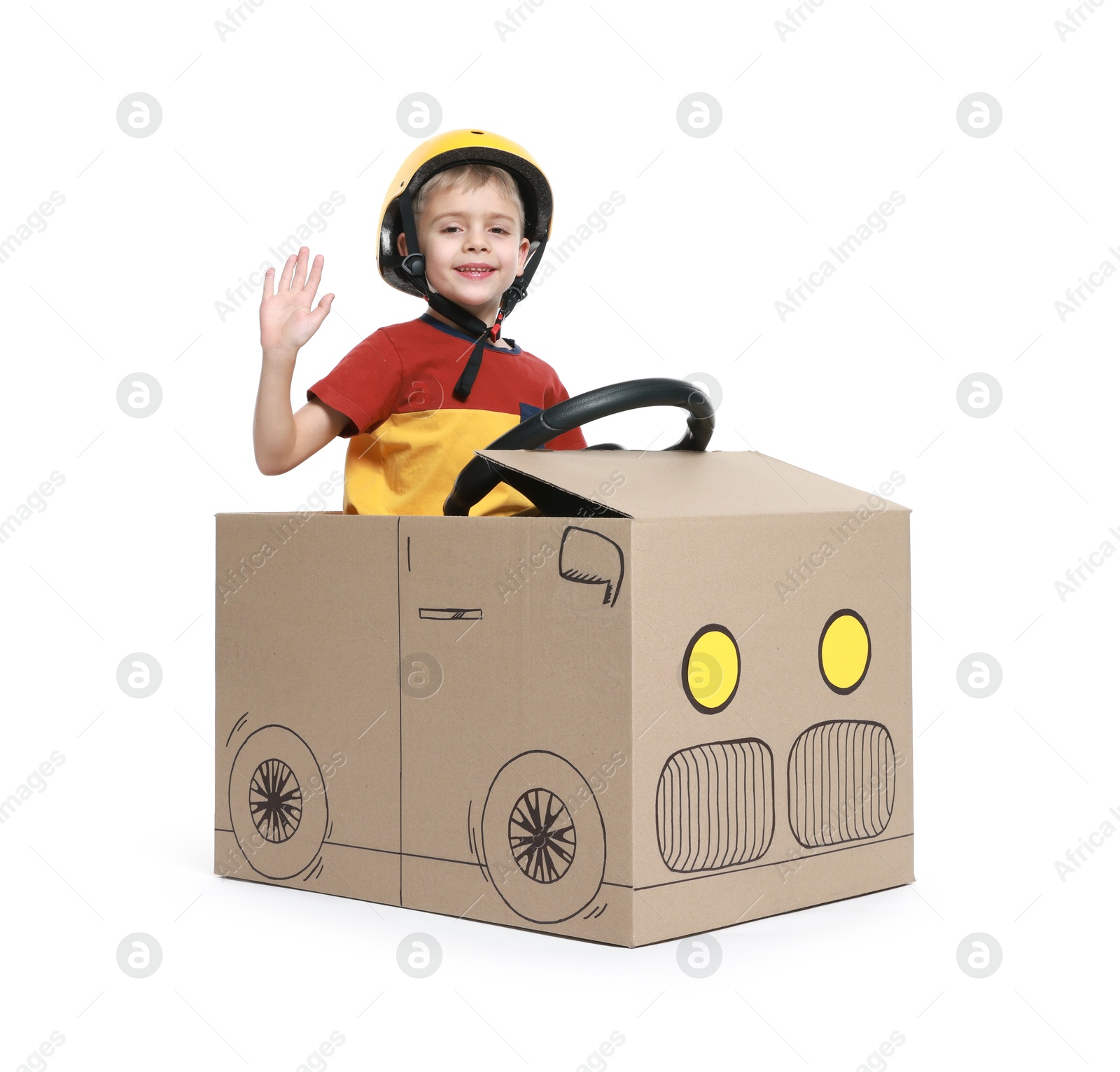 Photo of Little boy waving while driving car made of cardboard on white background