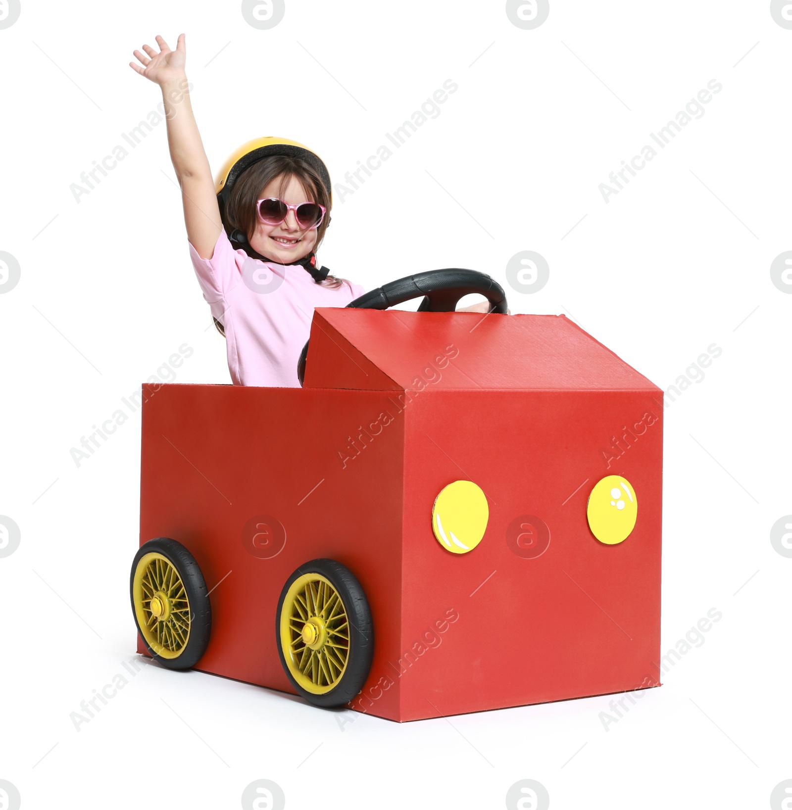 Photo of Little girl waving while driving car made with cardboard on white background