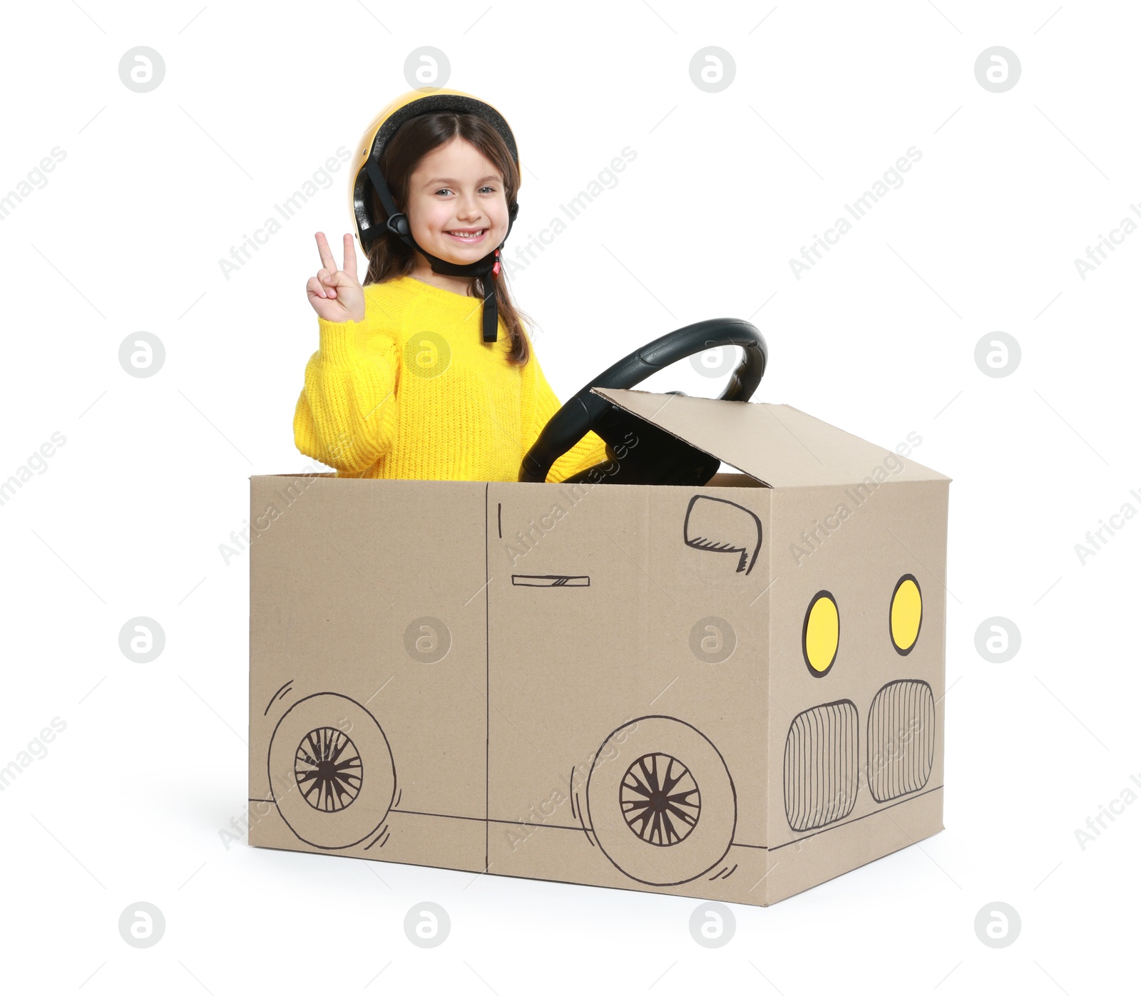 Photo of Little girl showing V-sign while driving car made with cardboard on white background