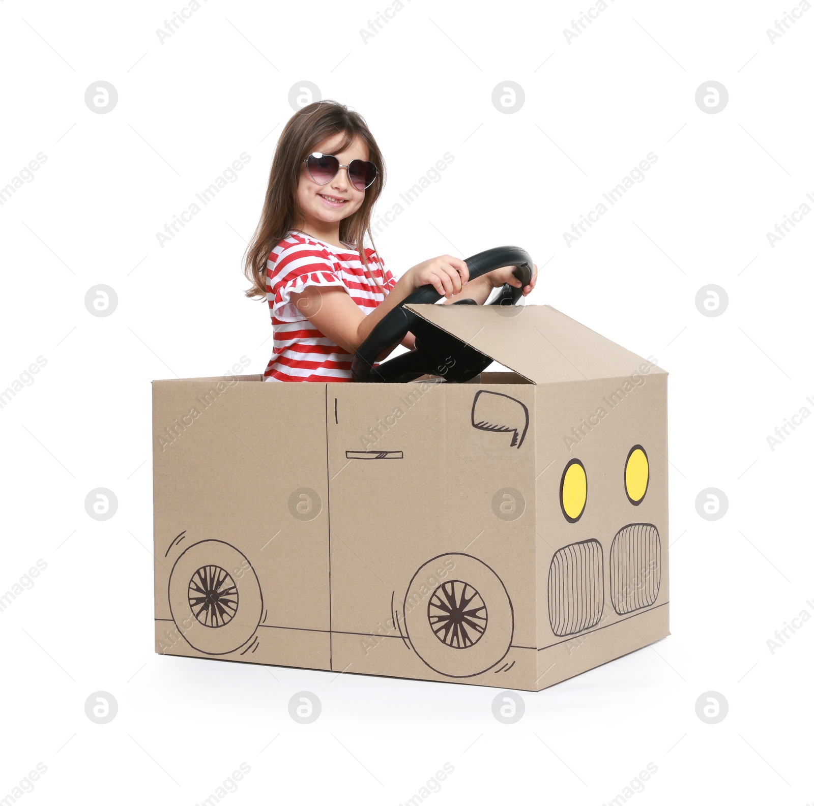 Photo of Little girl in sunglasses driving car made with cardboard on white background