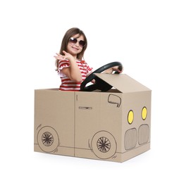 Photo of Little girl waving while driving car made with cardboard on white background