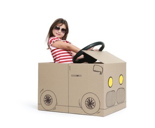 Photo of Little girl in sunglasses driving car made with cardboard on white background