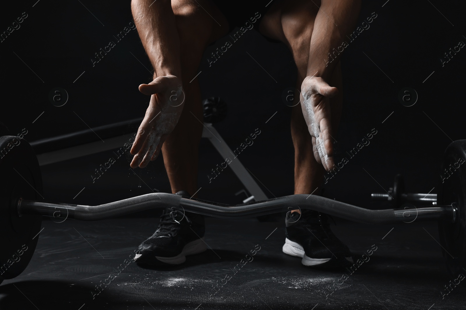 Photo of Man clapping hands with talcum powder before training with barbell in gym, closeup