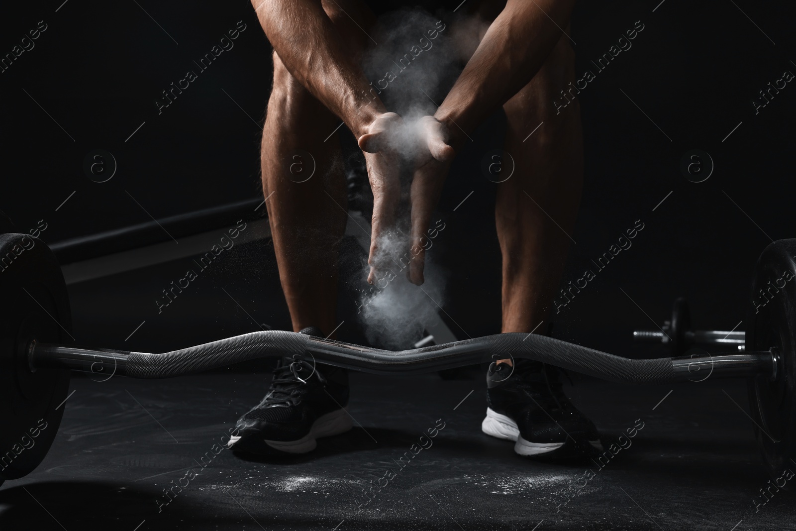 Photo of Man clapping hands with talcum powder before training with barbell in gym, closeup