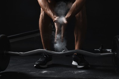 Photo of Man clapping hands with talcum powder before training with barbell in gym, closeup