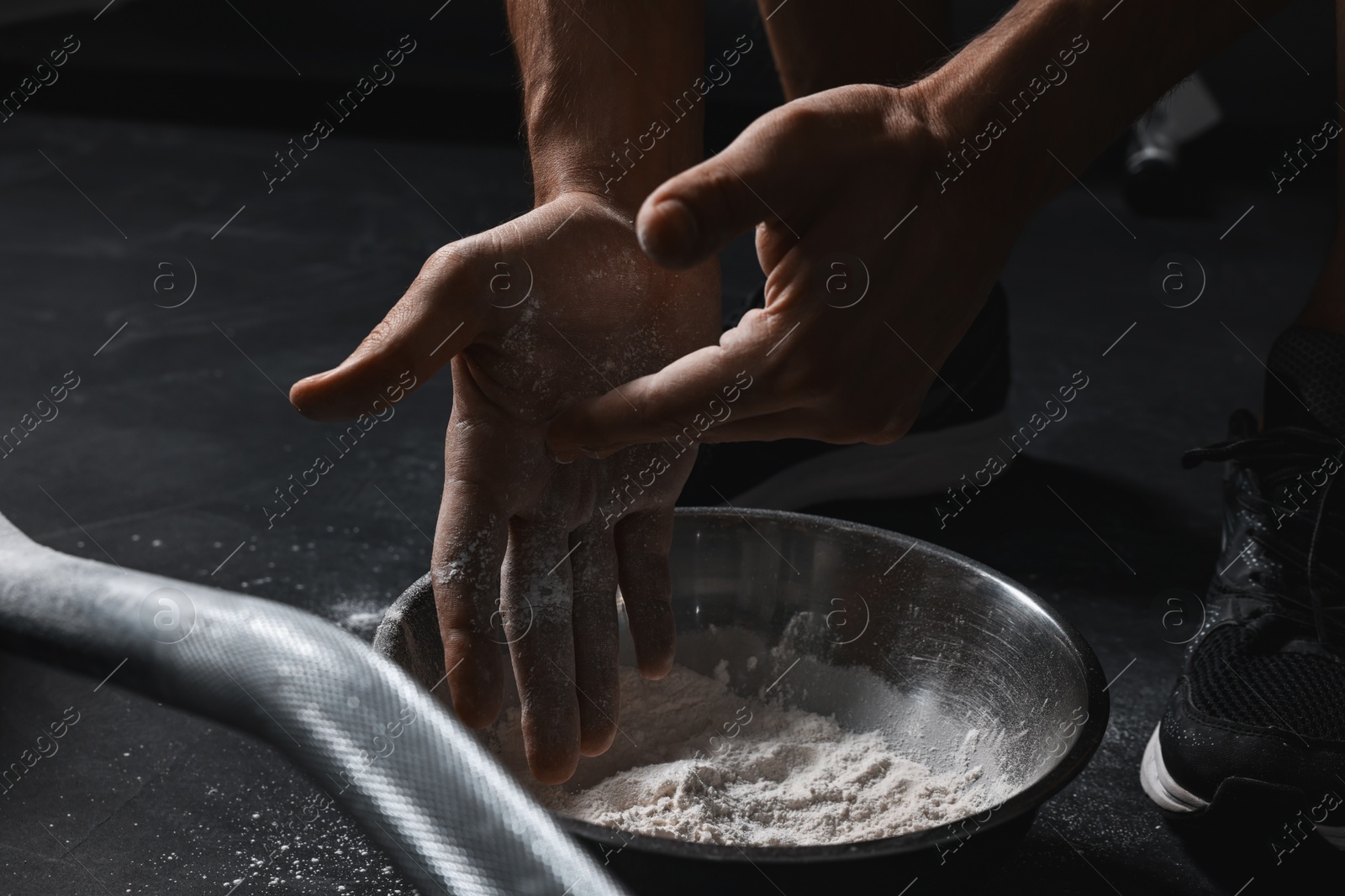 Photo of Man applying talcum powder onto his hands above bowl before training with barbell in gym, closeup