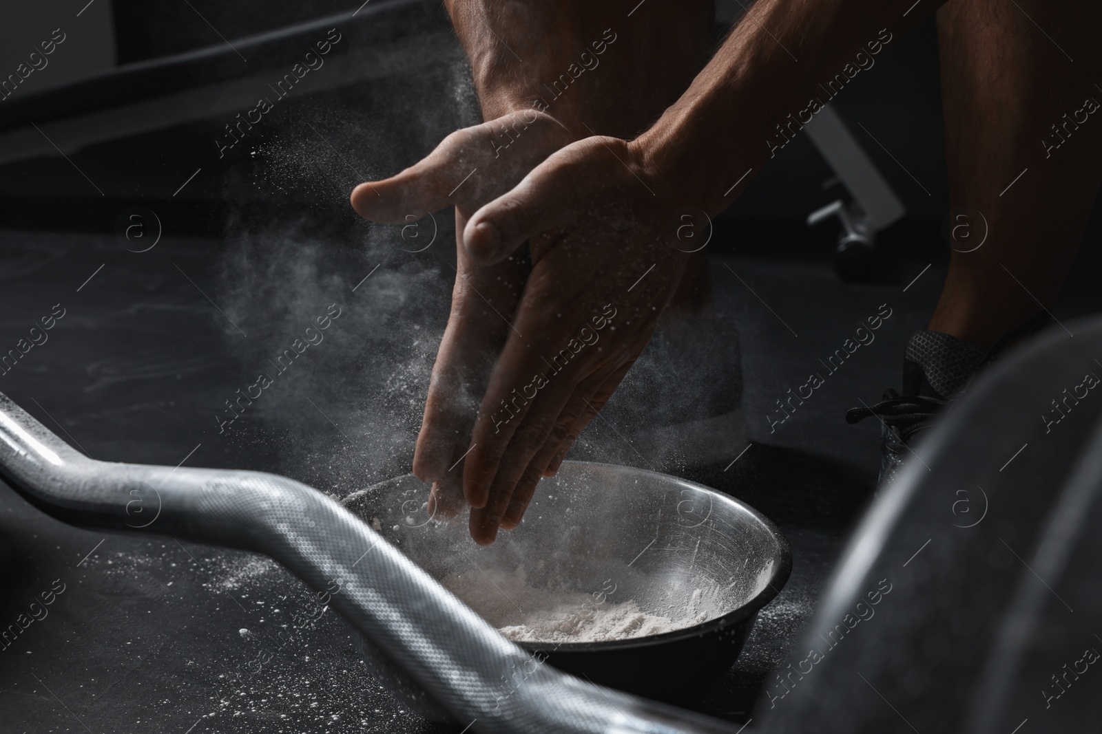 Photo of Man clapping hands with talcum powder before training with barbell in gym, closeup