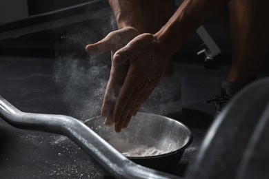 Photo of Man clapping hands with talcum powder before training with barbell in gym, closeup