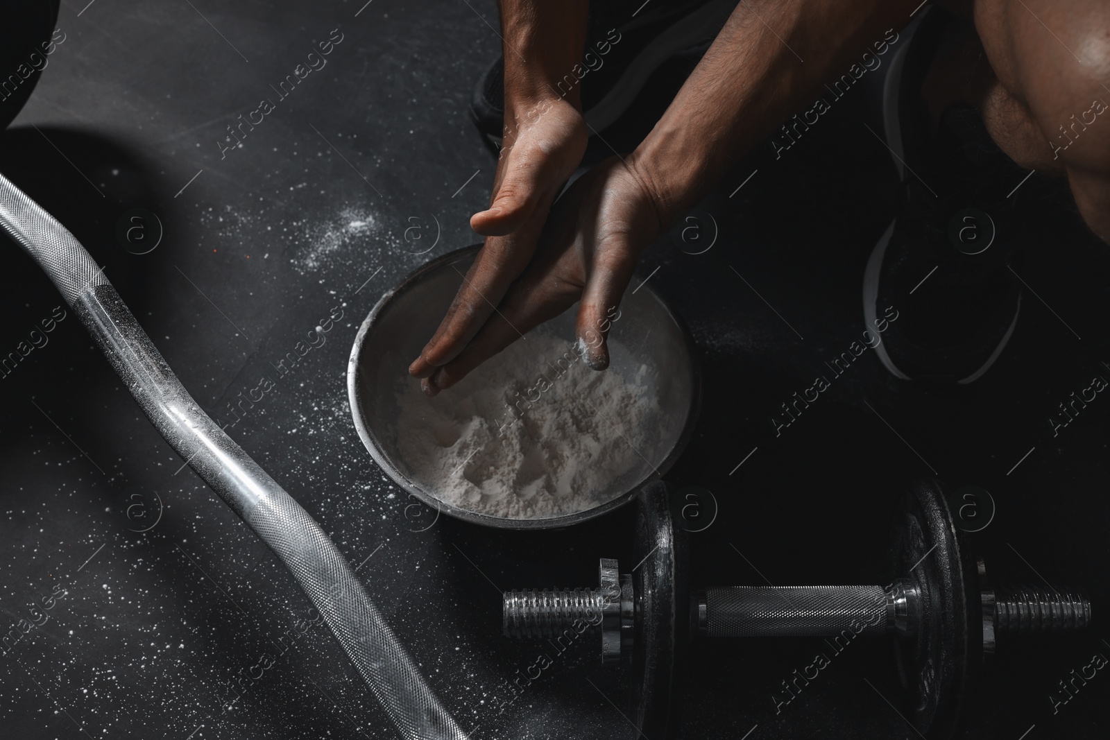 Photo of Man applying talcum powder onto his hands above bowl before training with barbell in gym, closeup