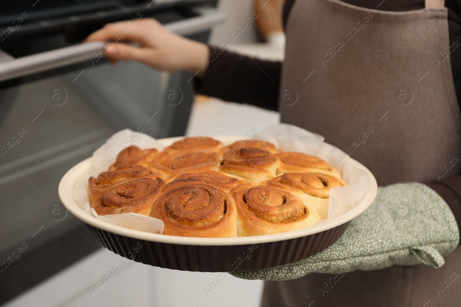 Photo of Woman with delicious cinnamon rolls near oven indoors, closeup