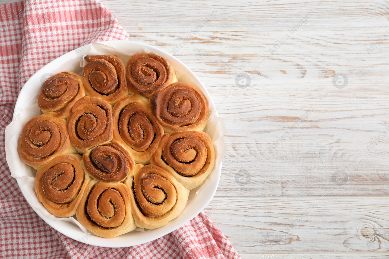 Photo of Freshly baked cinnamon rolls on light wooden table, top view. Space for text