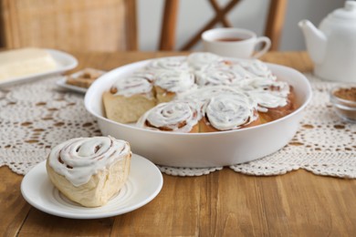 Delicious frosted cinnamon rolls on wooden table indoors, closeup