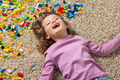 Photo of Cute girl lying near building blocks on carpet at home