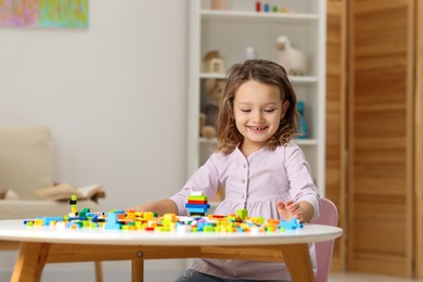 Photo of Cute girl playing with building blocks at white table indoors. Space for text