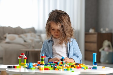 Photo of Cute girl playing with building blocks at white table indoors