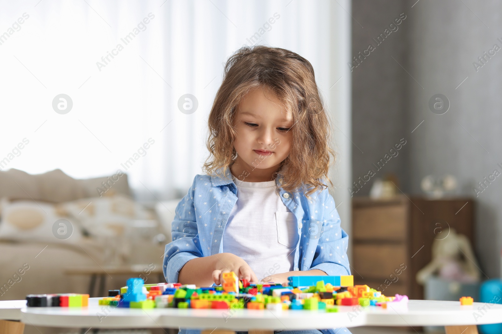 Photo of Cute girl playing with building blocks at white table indoors