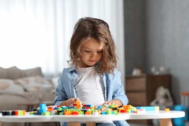 Photo of Cute girl playing with building blocks at white table indoors