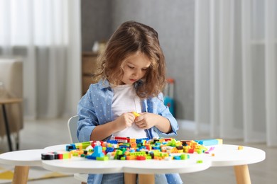 Photo of Cute girl playing with building blocks at white table indoors