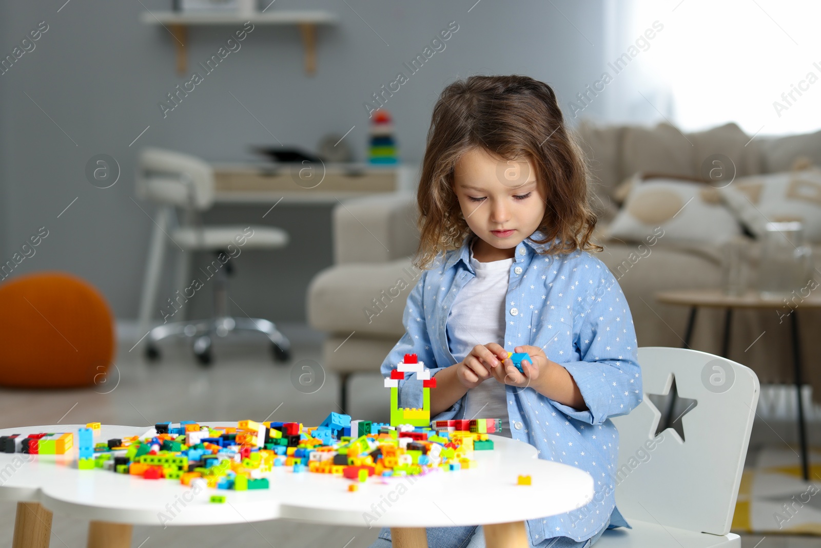 Photo of Cute girl playing with building blocks at white table indoors