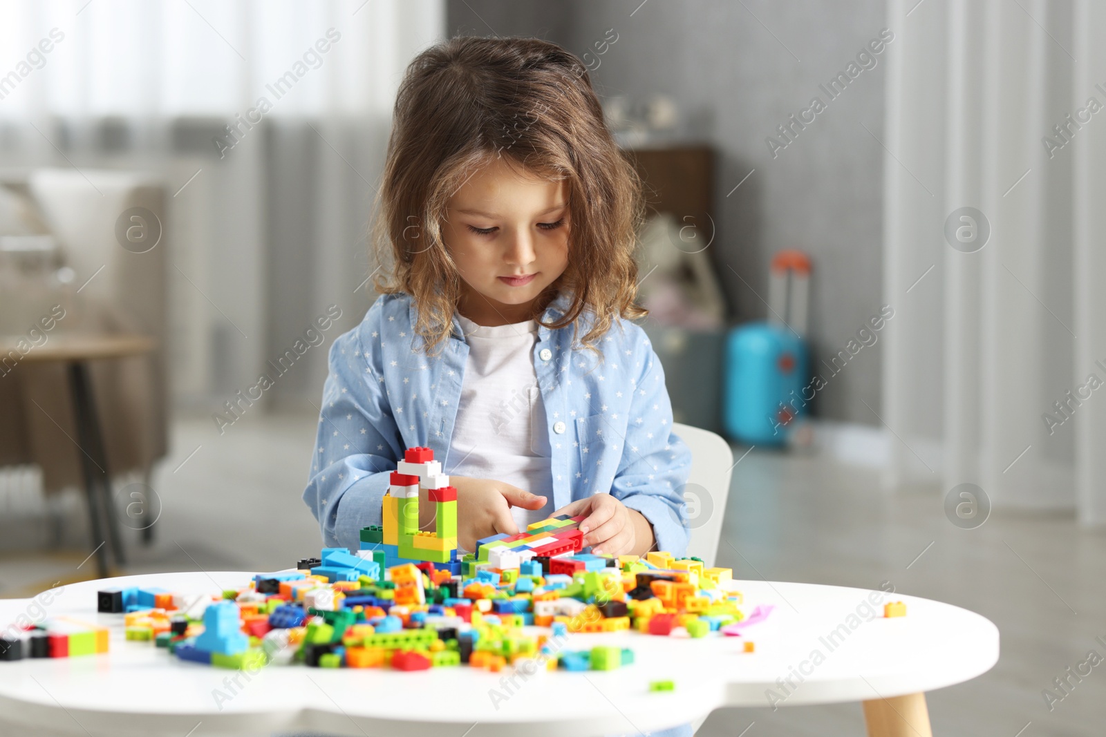 Photo of Cute girl playing with building blocks at white table indoors