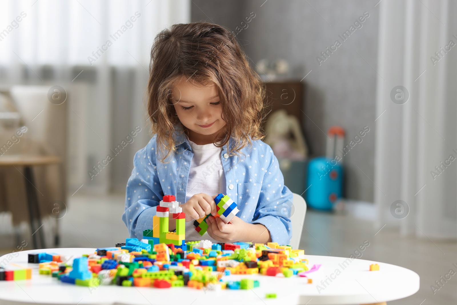 Photo of Cute girl playing with building blocks at white table indoors