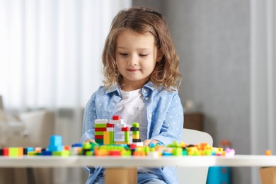 Photo of Cute girl playing with building blocks at white table indoors