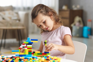 Photo of Cute girl playing with building blocks at white table indoors