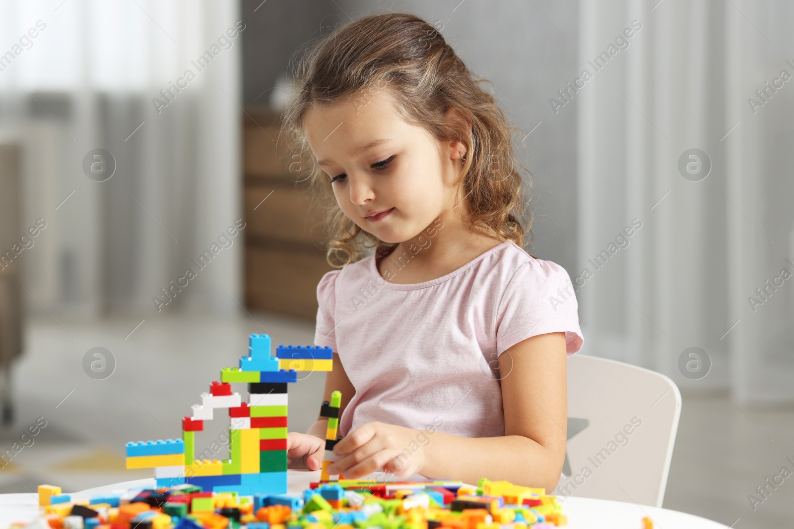 Photo of Cute girl playing with building blocks at white table indoors