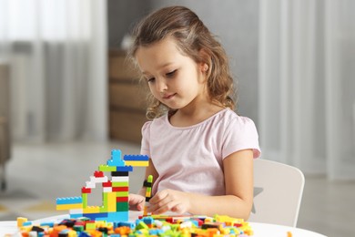 Photo of Cute girl playing with building blocks at white table indoors