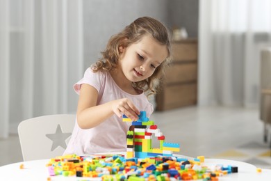 Photo of Cute girl playing with building blocks at white table indoors