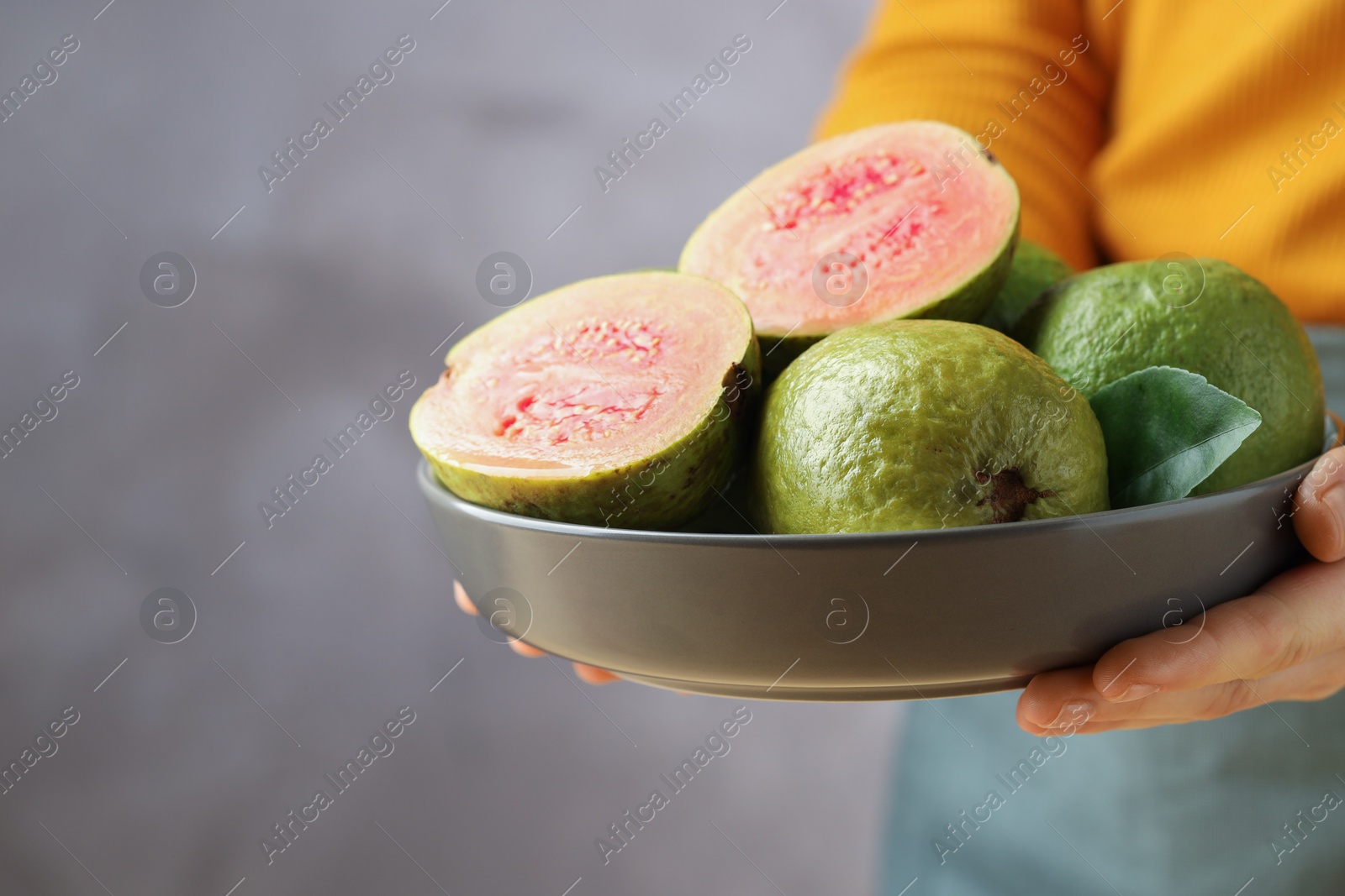 Photo of Woman with bowl of fresh guava fruits on blurred grey background, closeup. Space for text