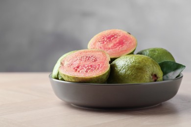 Photo of Fresh guava fruits in bowl on wooden table against blurred grey background, closeup