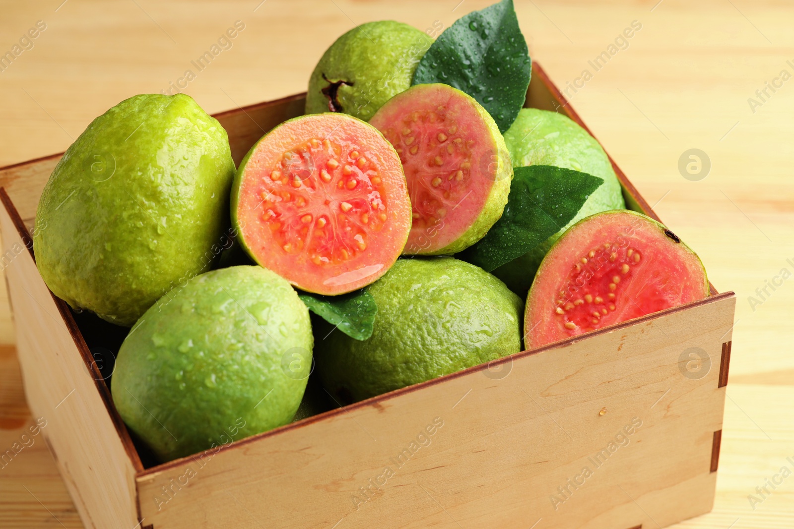 Photo of Fresh cut and whole guava fruits in wooden crate on table, closeup