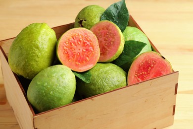 Photo of Fresh cut and whole guava fruits in wooden crate on table, closeup