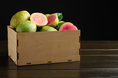 Fresh cut and whole guava fruits in wooden crate on dark table against black background, closeup