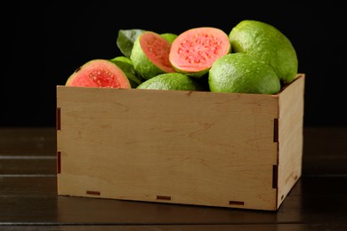 Fresh cut and whole guava fruits in wooden crate on dark table, closeup