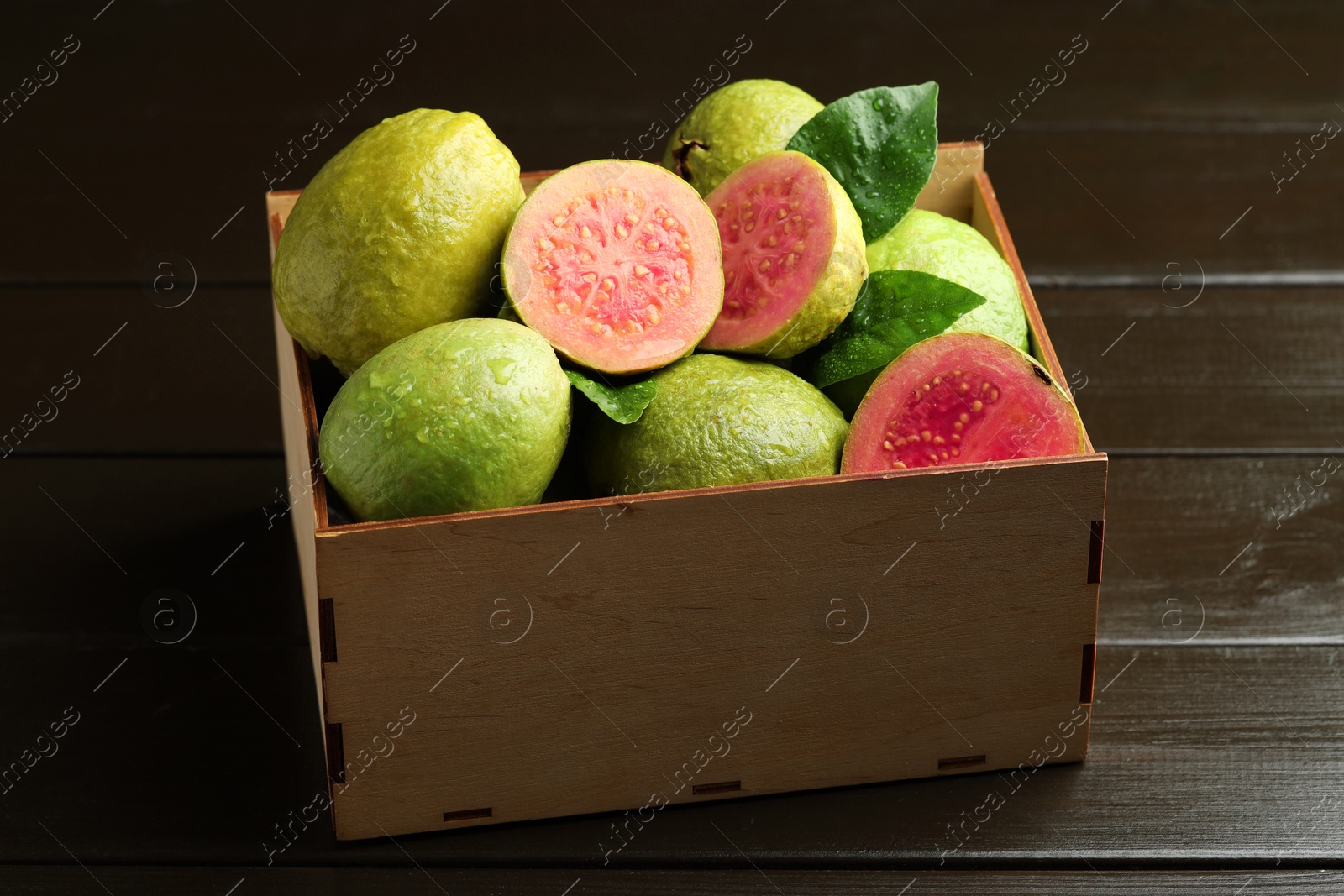 Photo of Fresh cut and whole guava fruits in wooden crate on dark table, closeup