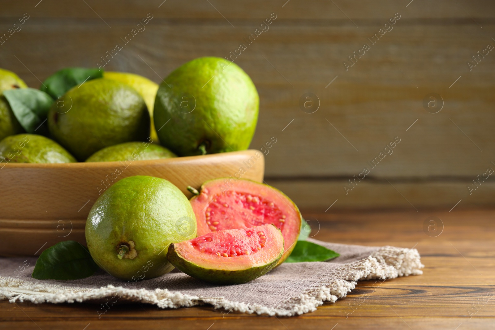 Photo of Fresh cut and whole guava fruits on wooden table, closeup. Space for text