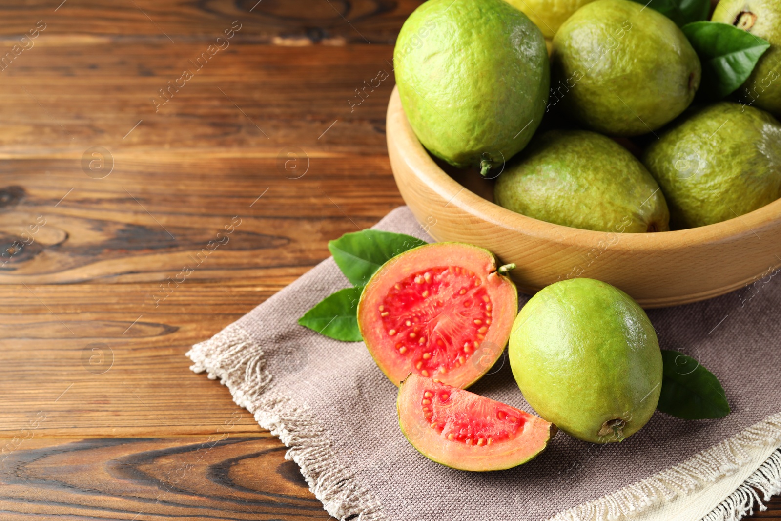 Photo of Fresh cut and whole guava fruits on wooden table. Space for text